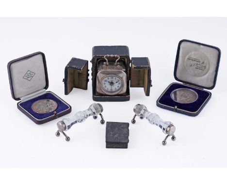 A white metal cased late 19th Century/early 20th Century travelling alarm clock, the white enamel dial with Arabic numerals i