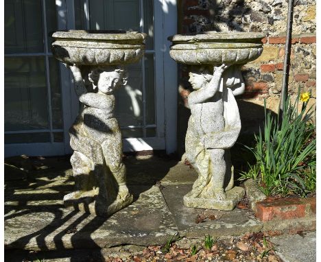 
	
		A pair of stone composition figural planters or bird baths, 20th century, each with a putto raising a lobed circular bas