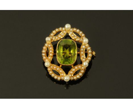 An Edwardian gold coloured metal peridot and seed pearl oval brooch of Art Nouveau Design, the central baguette cut stone +/-