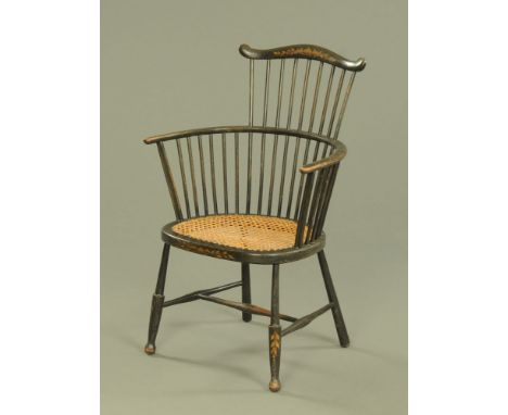 An ebonised two tier stick back tub shaped armchair, the crest rail gilded with leaves and with caned seat on turned legs.  B
