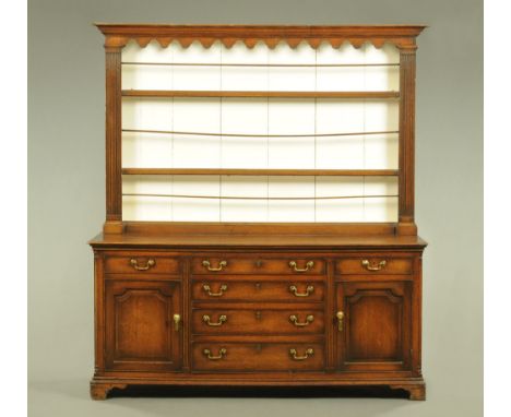 A George III oak dresser with Delft rack, with moulded cornice and shaped apron above a series of white painted shelves flank