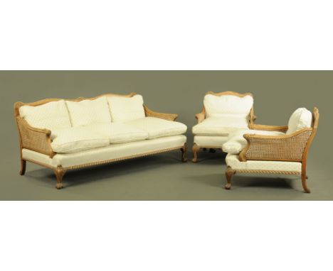 A walnut framed bergere lounge suite, comprising two chairs and settee, each piece with carved exposed showframe and raised o