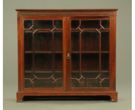 An Edwardian mahogany glazed bookcase, with moulded edge above a blind fretwork carved frieze and pair of glazed doors with w