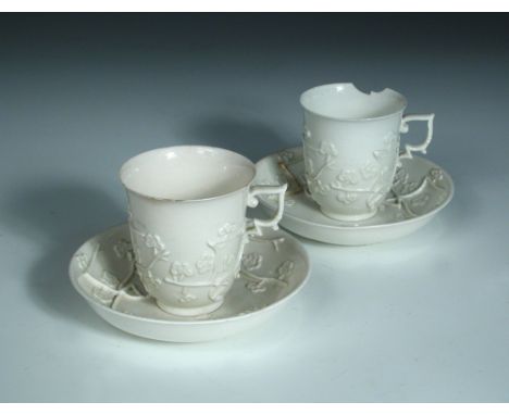 A pair of 18th century St Cloud white glazed cups and saucers, each moulded with three sprays of cherry blossom in relief in 