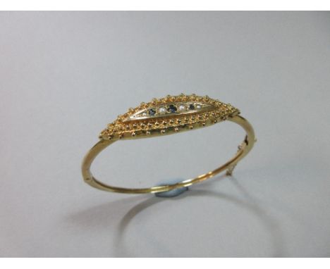 A 9ct gold sapphire and pearl hinged bangle, set to the front with a navette form plaque with a graduated line of alternating