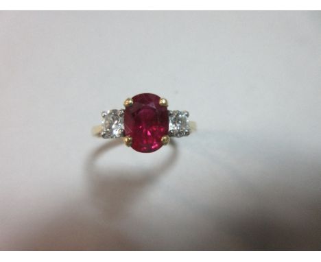 A ruby and diamond three stone ring set in 18ct gold, the oval cut ruby four claw set between two round brilliant cut diamond