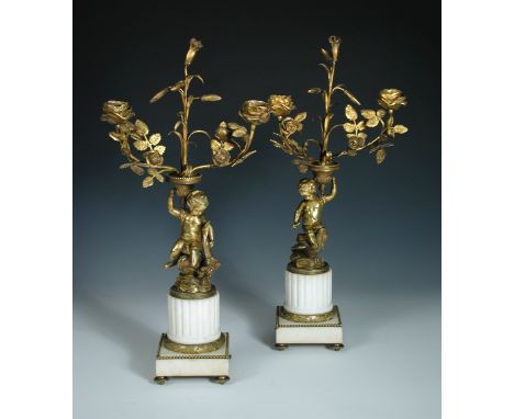A pair of 19th century ormolu twin light candelabra, each modelled as a putto sitting astride a bird and supporting the flowe