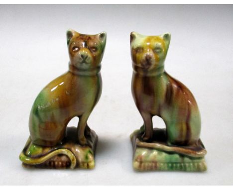 A pair of Whieldon ware cats, the seated felines facing each other on cushion bases, the dripping glazes in aubergine, green 
