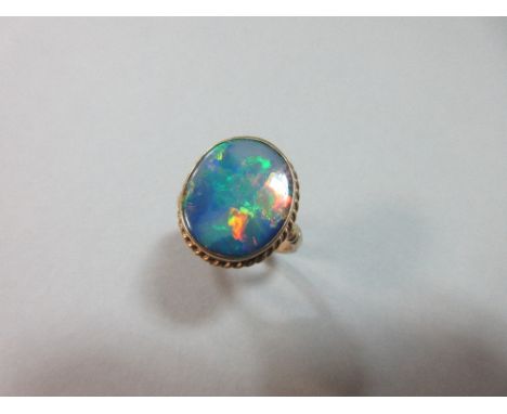 A black opal single stone ring, the oval flat cut opal, length 15mm, displaying a rainbow range of colour - blue, green, red,