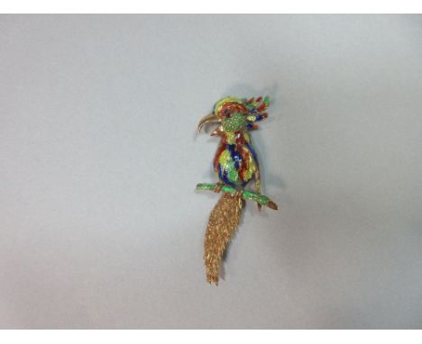 An enamelled exotic bird brooch, the bird perched on a green enamelled branch, polished beak open, extravagant textured tail 