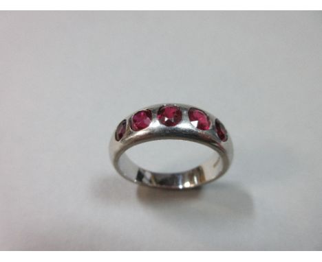 A modern 18ct white gold and ruby five stone ring,  the continuous chunky D-section shank, slightly tapered to the back and r