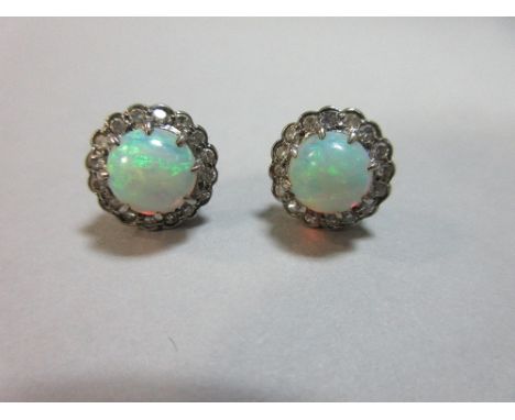 A pair of opal and diamond earstuds, each with a round cabochon opal in a scalloped edge border of single cut diamonds, in un