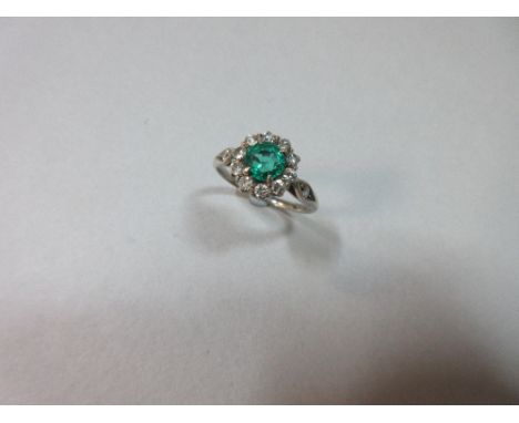 A diamond and synthetic emerald cluster ring, the round mixed cut emerald four claw set in a border of ten round brilliant cu