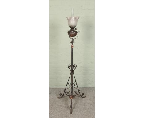 A wrought iron standard oil lamp with glass shade and adjustable stem  
