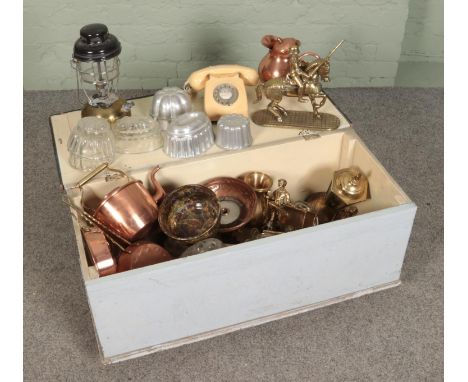 An ottoman full of mixed metal and glassware items including Tilley lamp, copper and glass jelly molds, Bakelite phones, bras