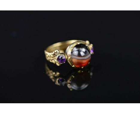 A LATE GEORGIAN GOLD MEMORIAL RING, designed as a central circular banded agate cabochon, centre cabochon is of a hinged fitt