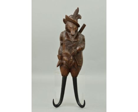 A 19TH CENTURY BLACK FOREST CARVED FOX MUSICAL COAT HOOK, modelled as wearing feathers in his hat, glass eyes, coat, rifle sl