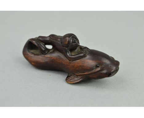 A MEIJI PERIOD CARVED WOODEN NETSUKE, in the form of a fish surmounted by a monkey, both with black glass eyes, inset disc wi
