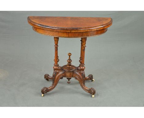 A VICTORIAN BURR WALNUT DEMI LUNE FOLD OVER CARD TABLE, revealing a green baize interior, on four cylindrical supports united