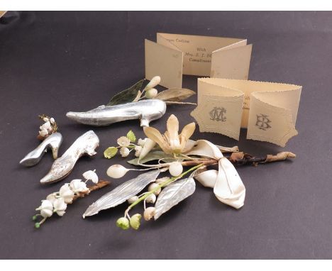 A box containing local bygone wedding cake decorations including silver shoes, faux lily of the valley and compliment cards, 