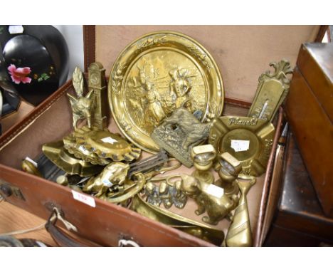 A vintage brown card suitcase containing a selection of miscellaneous brasswares, including fox mask door knocker, bell weigh