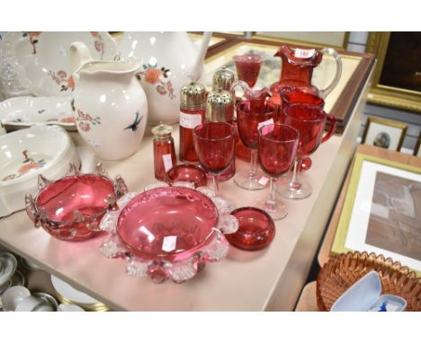 A selection of cranberry glass and a ruby glass jug, amongst the cranberry are sugar sifters, glasses, jugs and bowls.
