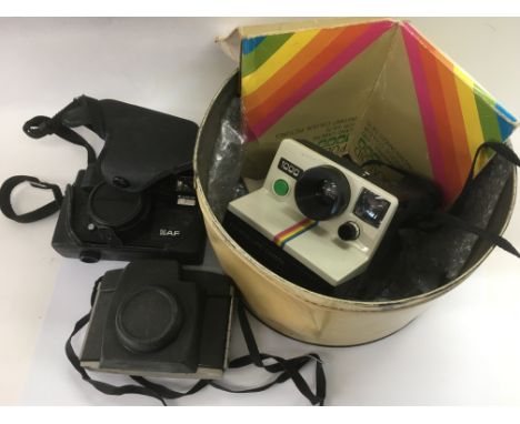 A tin containing a vintage Polaroid camera and two others.
