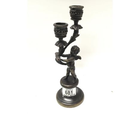 A bronzed candle stick with scroll branches supported by a cherub. Height 24cm.