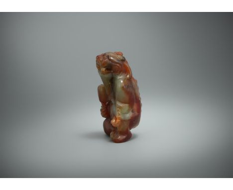 A Chinese mottled jade model of a seated mythical beast, Ming dynasty, carved holding a club in its right hand, 4.9cm highPro