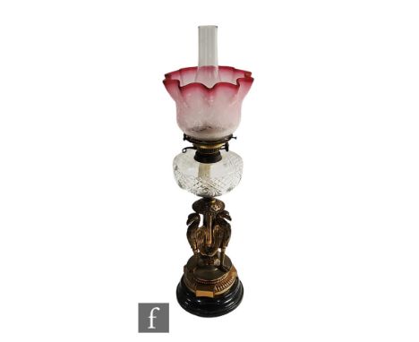 A Victorian brass oil lamp, the cut glass reservoir over a base supported by three winged Griffins with floral ruby shade and