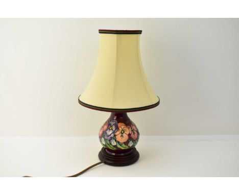 MOORCROFT; a modern tube lined pottery lamp, decorated with pansies on burgundy ground, on wooden base, with original lampsha