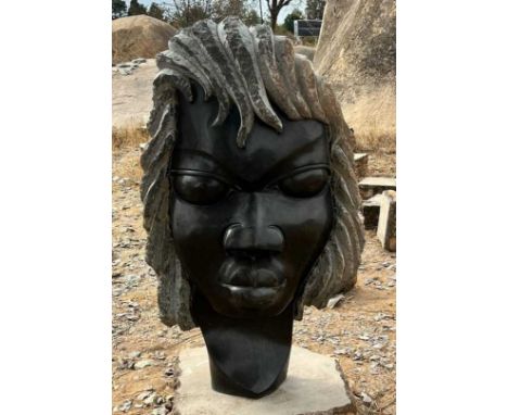 M AUGUSTINE; a large African carved springstone and serpentine sculpture, modelled as a figure with long hair, signed verso, 