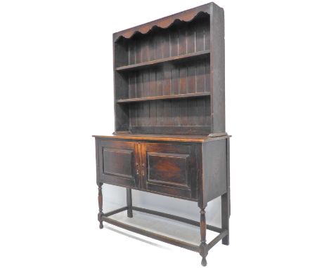 An early 20th century oak dresser; the shelved superstructure above two fielded panel doors, raised on turned front legs unit