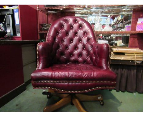 A Georgian style red leather button back library swivel desk armchair with brass stud decoration over castors 