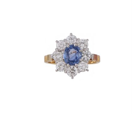 A SAPPHIRE AND DIAMOND CLUSTER RING  LONDON 1984  The oval cut sapphire within a surround of brilliant cut diamonds, approxim