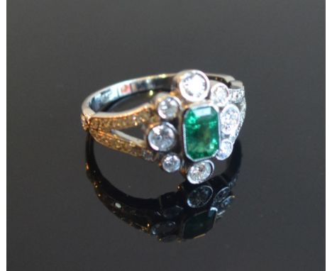 An 18ct. White Gold Emerald and Diamond Ring with a central emerald surrounded by diamonds within a pierced setting