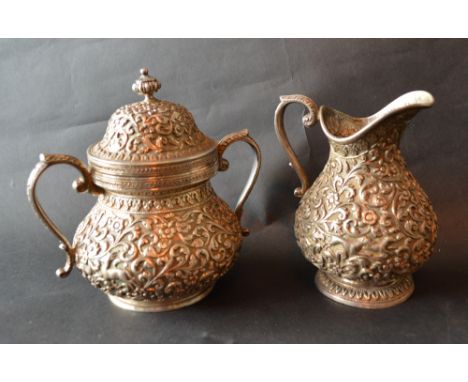 An Indian White Metal Cream Jug decorated in relief with a foliate scroll design together with a matching two handled covered