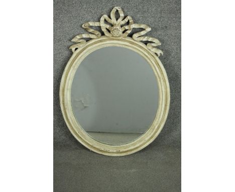 A vintage Continental grey painted and distressed oval mirror, with a carved frame and carved ribbon cresting. H.83 W.60cm. 