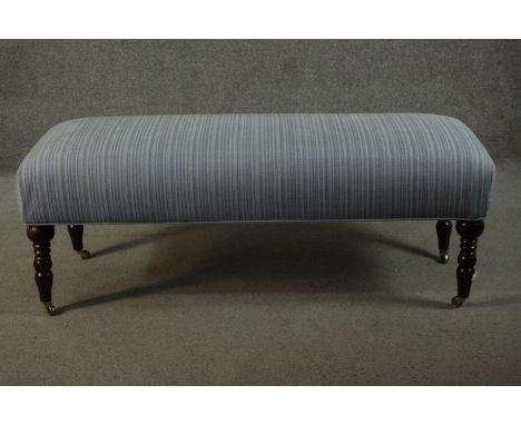 A Victorian style long stool, with an overstuffed seat upholstered in striped light blue fabric, on turned mahogany legs term