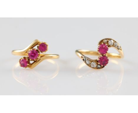 A yellow metal ruby and diamond ring, set with two round cut rubies in a cross over style shank, each side of the shank set w