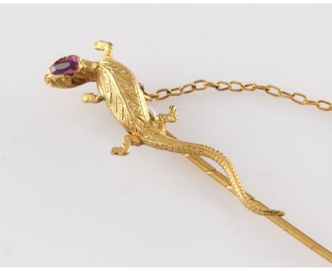 A yellow metal stick pin in the form of a lizard, the lizard having a red stone set to his head and the entire body being eng