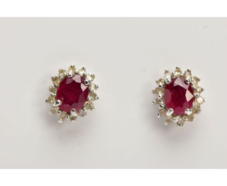 A PAIR OF 9CT WHITE GOLD CLUSTER EARRINGS, of an oval form, centring on an oval cut ruby, within a surround of single cut dia