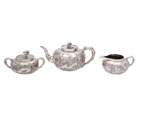 A Chinese silver three piece tea service, early 20th century, maker Wang Hing, Hong Kong, prunus blossom pattern with bamboo 