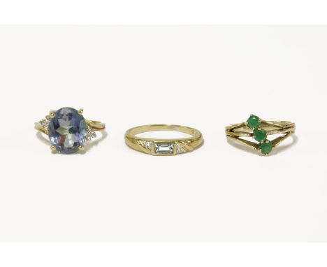 A 9ct gold three stone emerald ring, a gold oval cut sputtered topaz and diamond ring, marked 10k, and a gold baguette cut to