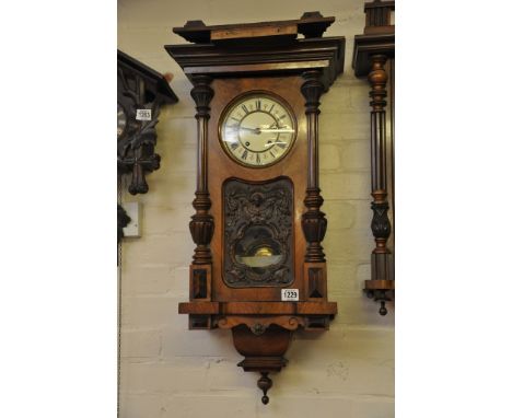 A walnut wall clock with an enamel dial and visible pendulum 