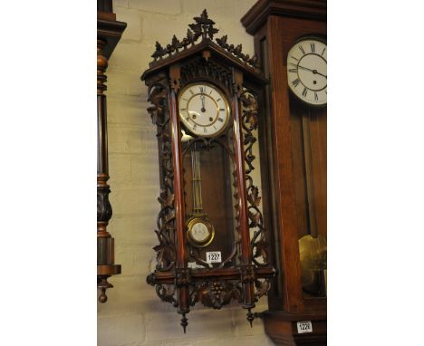 A finely carved continental wall clock the case with foliate open fret work with an enamel dial and visible pendulum 
