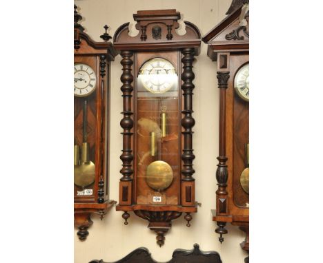 A walnut cased Vienna wall clock with an arched top the white enamel dial flanked by turned pilasters
