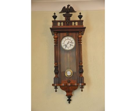 A walnut wall clock the case surmounted with an eagle above a white enamel dial and visible pendulum 