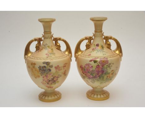 A pair of Royal Worcester twin handled vases decorated with flowers and foliage on a blush ivory ground with gilt details. He