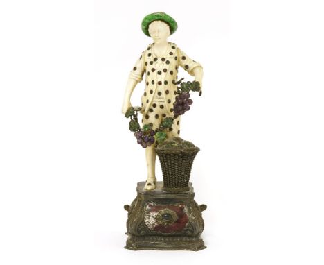 A German ivory figure, c.1900, depicting a street vendor holding grapes over a basket, with an enamel hat and 'jewelled' cost